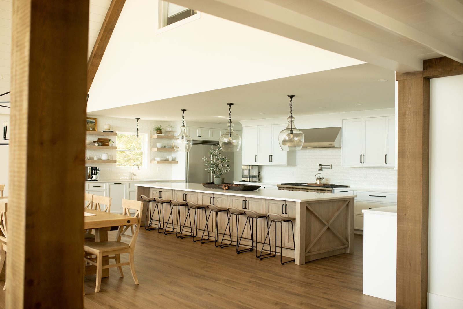 Great room with long dining table, iron chandeliers and the kitchen beyond